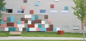 The image shows a bench in front of the side of a building which features colorful squares.