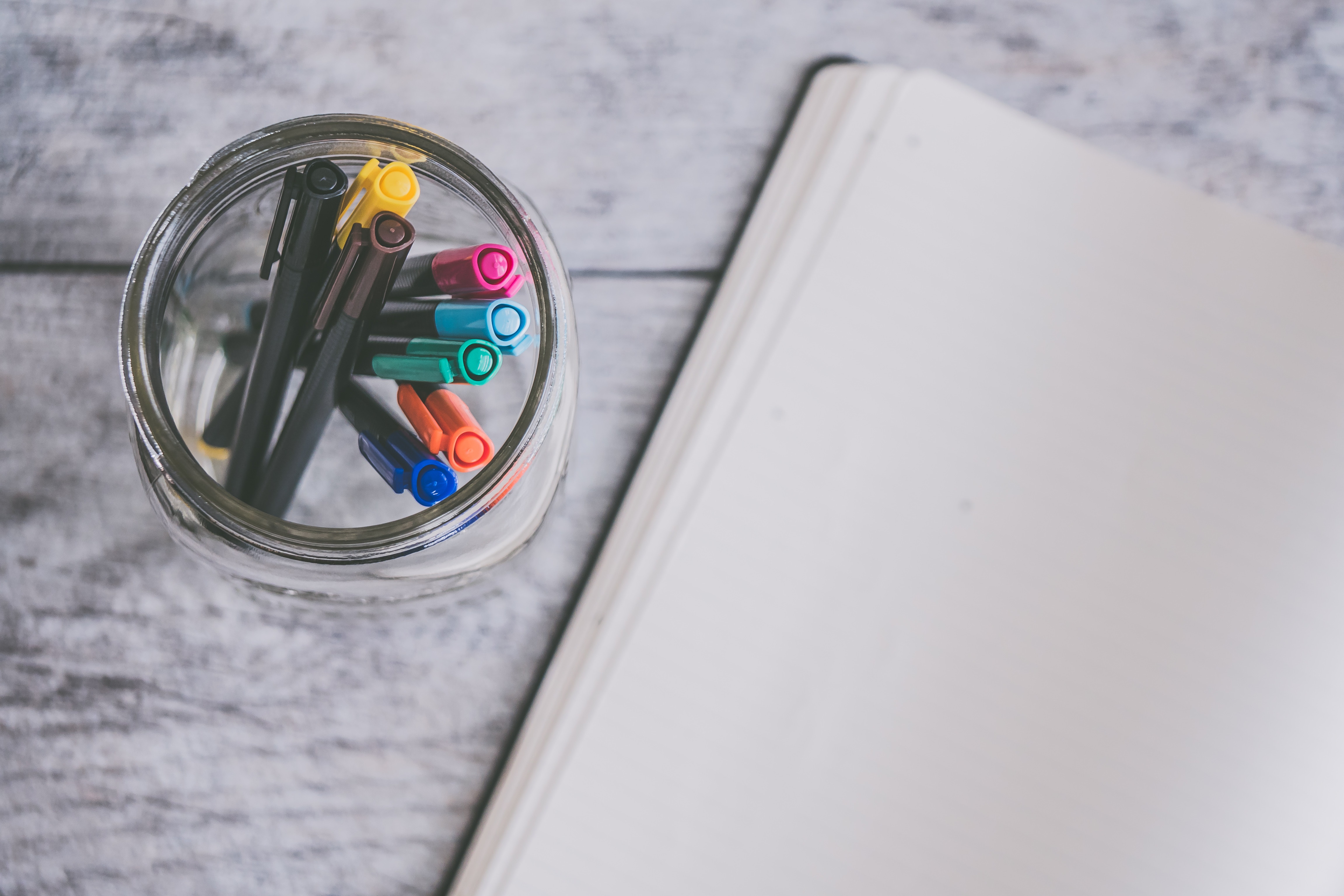 Image of assorted color markers in a glass jar next to a blank notebook
